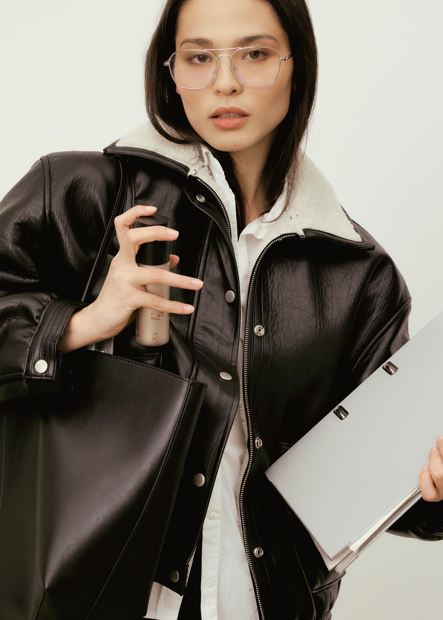 Femme portant une veste noire, tenant un flacon de soin Pômesse Paris, avec un sac et un ordinateur portable sous le bras