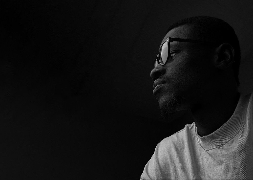 A person wearing headphones sits at a desk with a large curved monitor displaying graphic design software, surrounded by a laptop, smartphone, and potted plant, creating a modern workspace setup.
