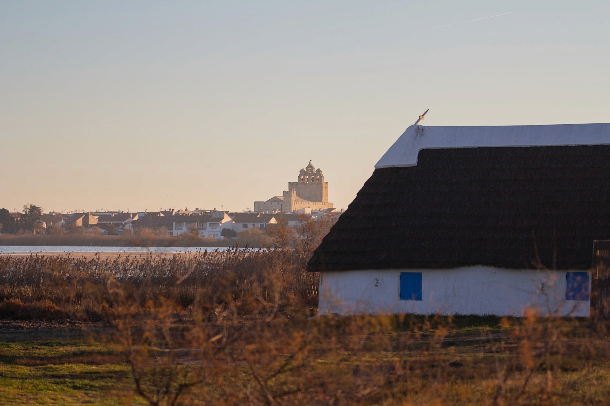 Photo du clocher des saintes maries de la mer avec une cabane de gardian au milieu de la nature en premier plan