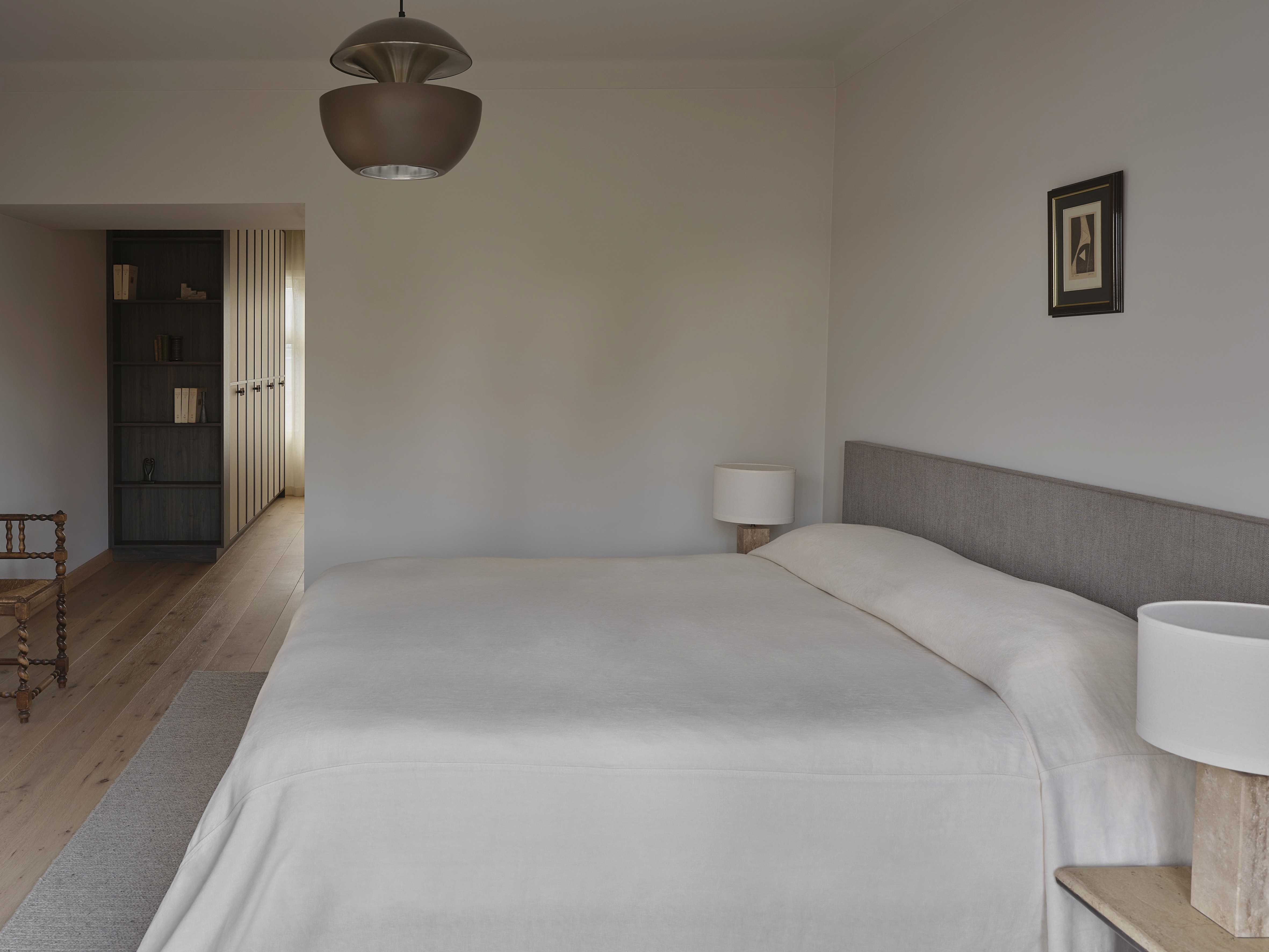 Master bedroom with brass pendant light, upholstered headboard, and darkwood and travertin nightstands
