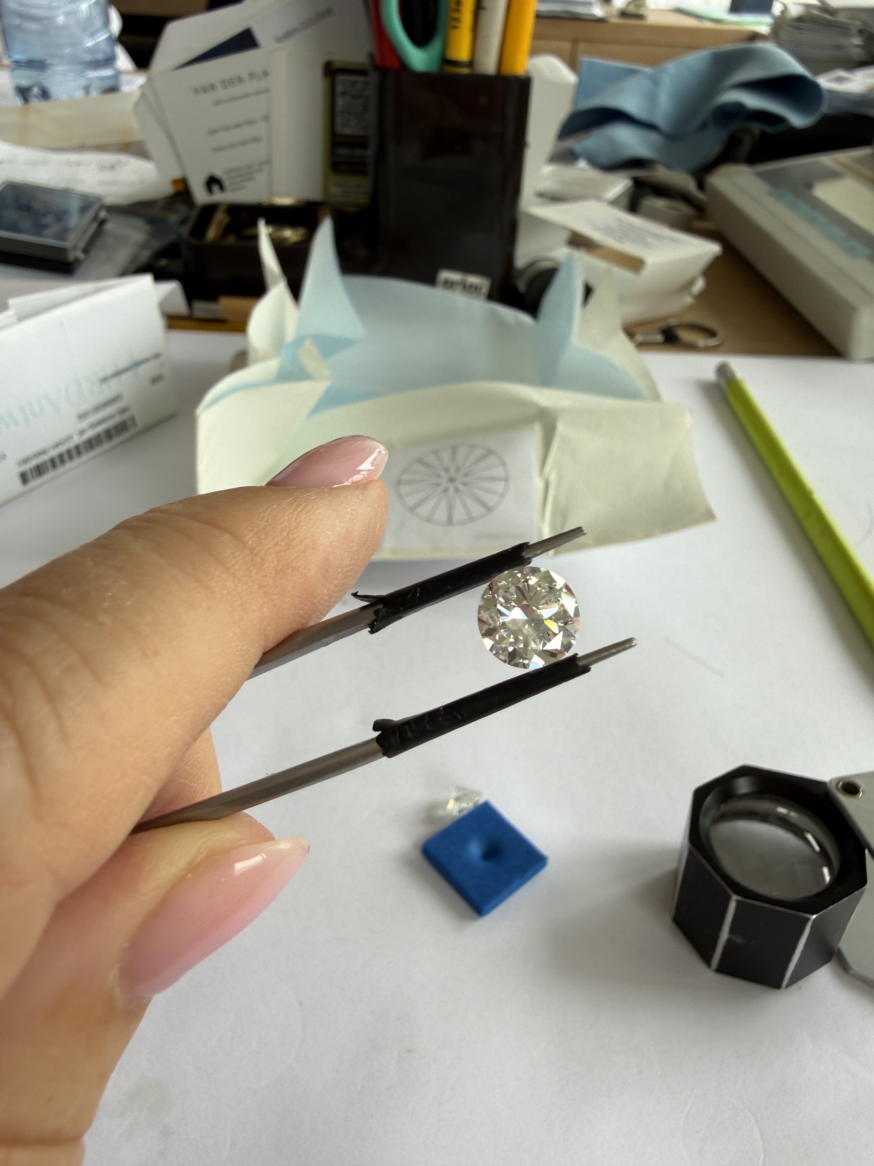 Rund diamant holdt i pincet over et diamantpapir på et sorteringsbord