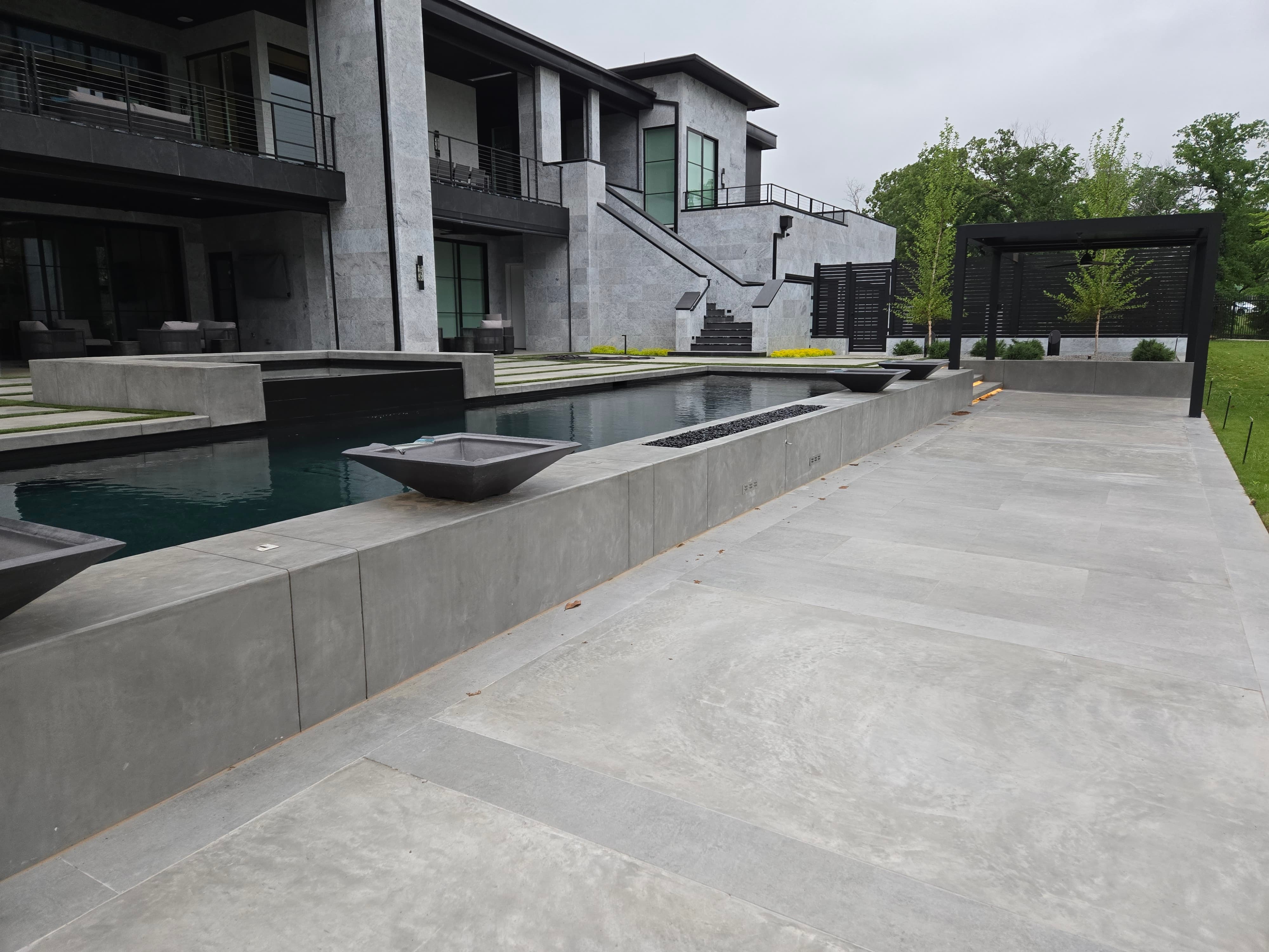 Negative-edge spa beside the pool with dark concrete decking and the modern Dallas home in the background