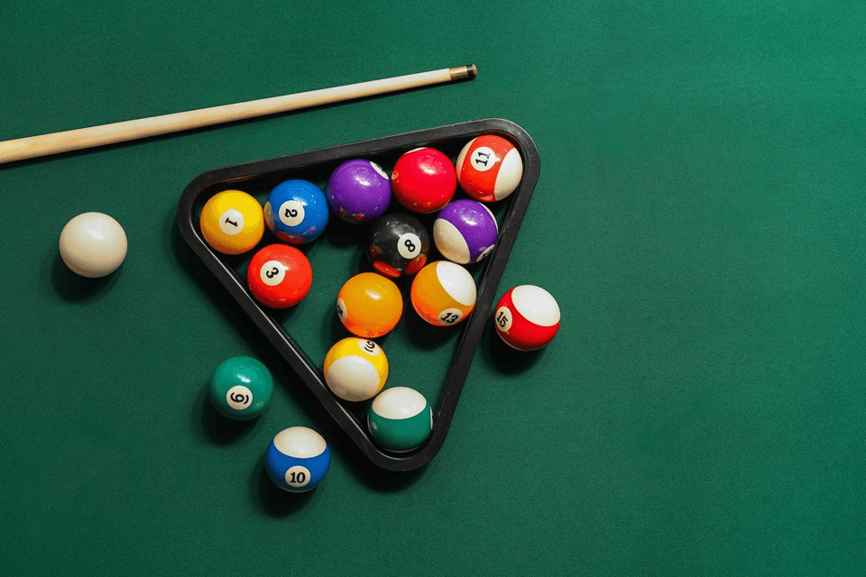 A triangle rack holds colorful billiard balls on a green felt table, with a cue stick resting nearby.