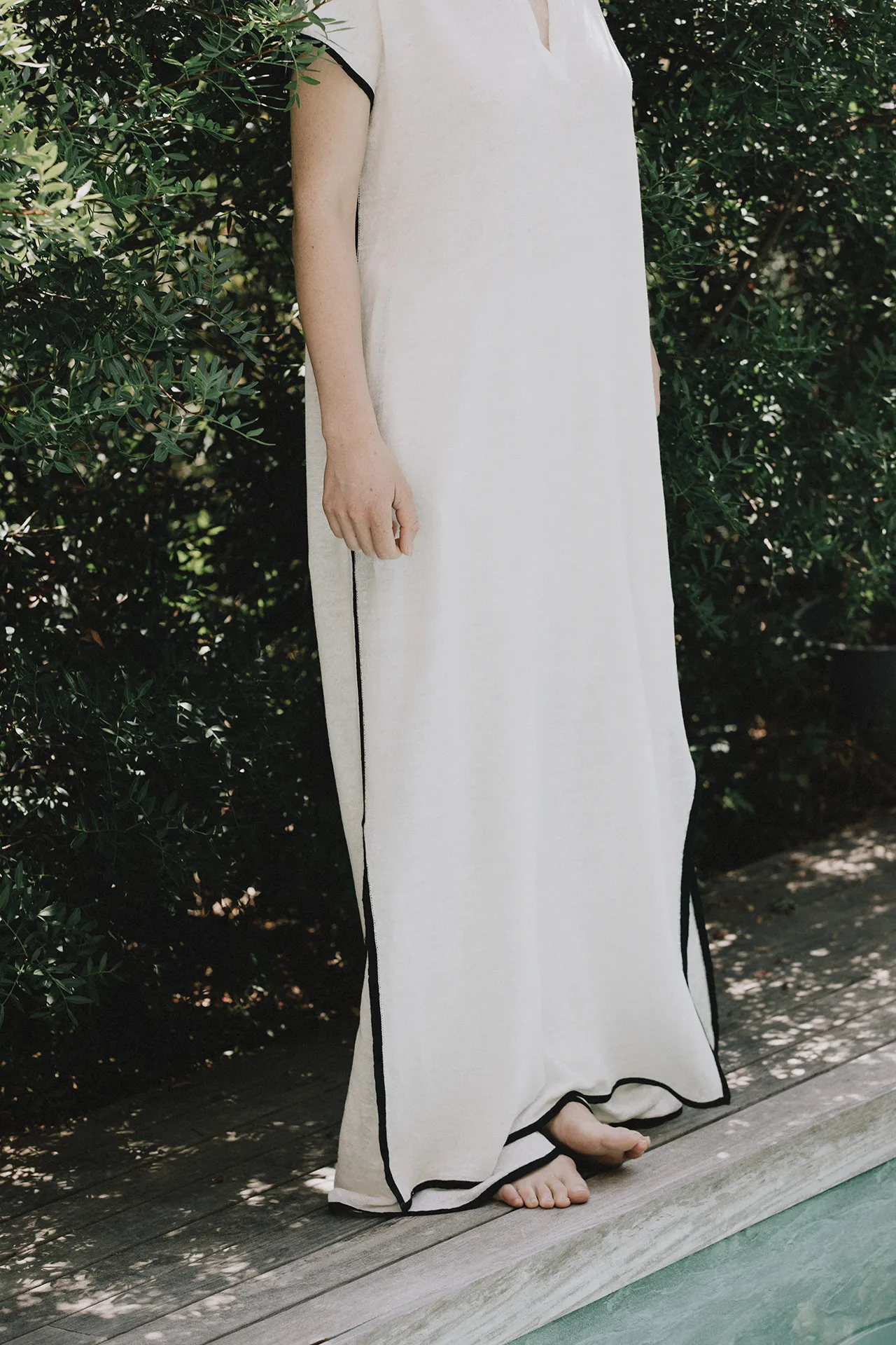 Detail view of Annapurna SS26 collection white fine-knit maxi dress featuring black trim along the hemline.