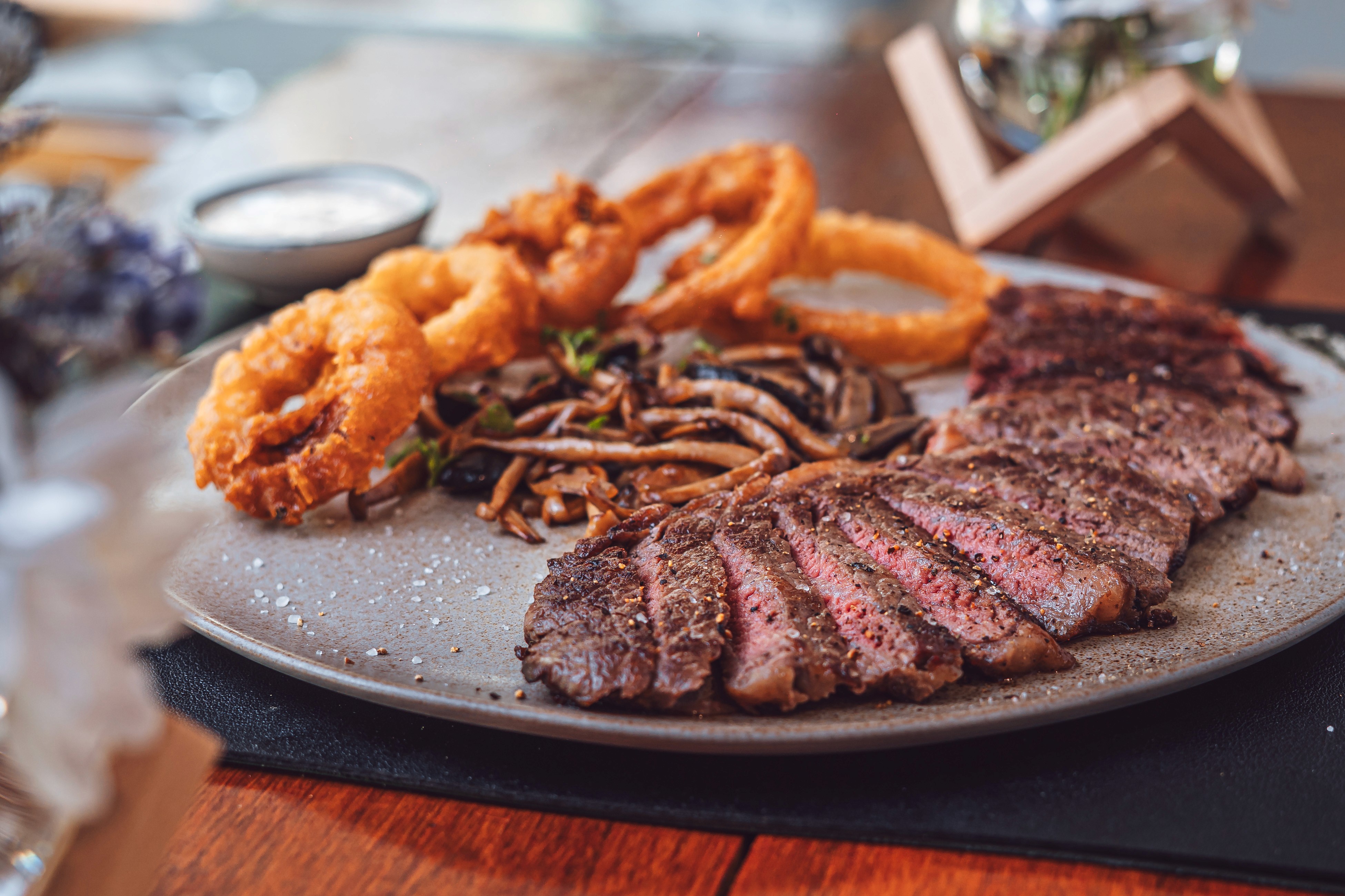 A tall stack of French toast or waffles, heavily drizzled with syrup and topped with slices of banana, dusted with powdered sugar, and served in dramatic, dark lighting.