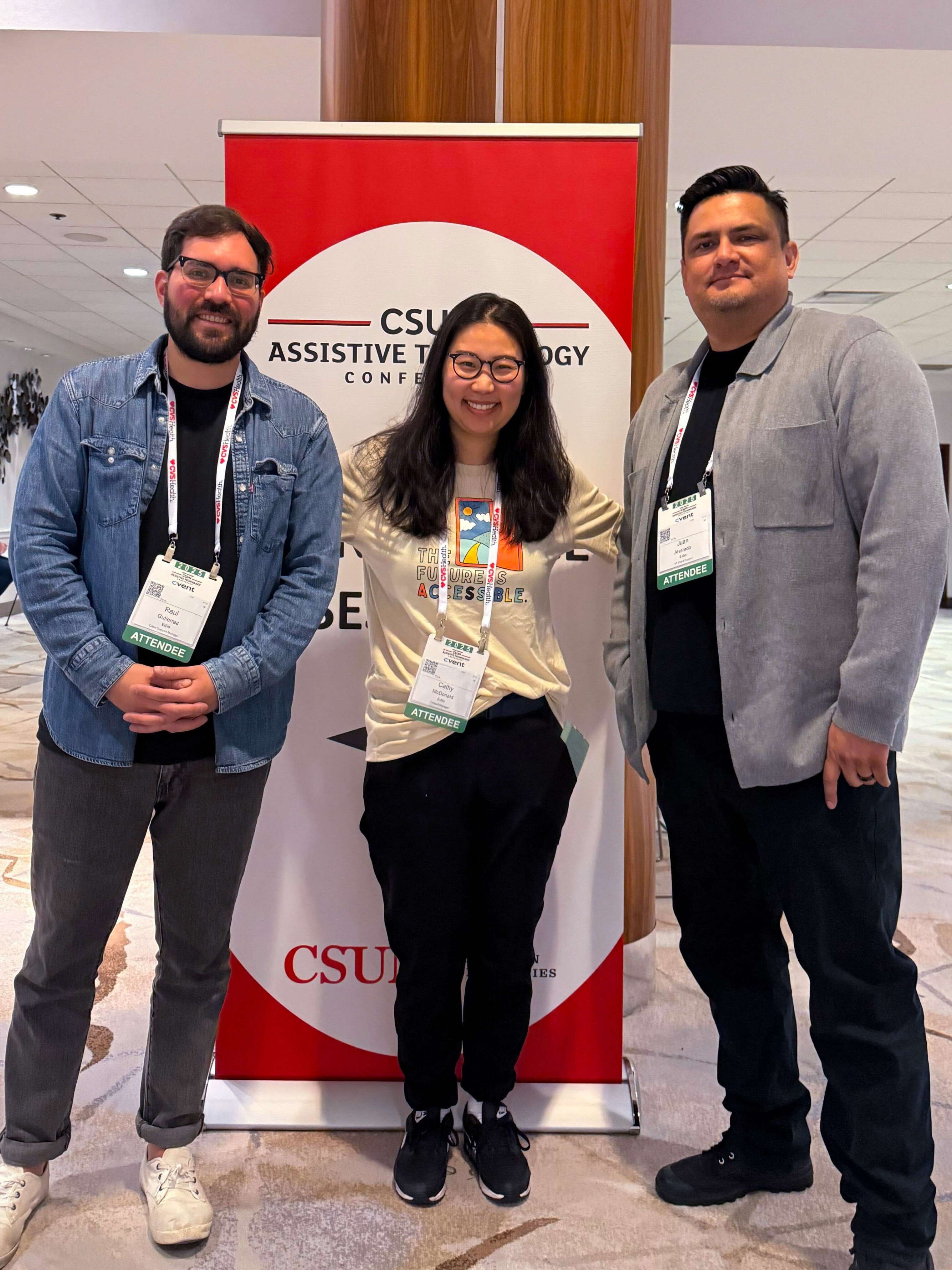 Three attendees smiling in front of a CSUN Assistive Technology Conference banner.