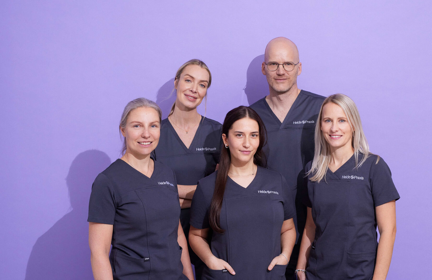 Das 5 köpfige Team der Heidepraxis in der Halbtotale vor mlila farbigen Hintergund