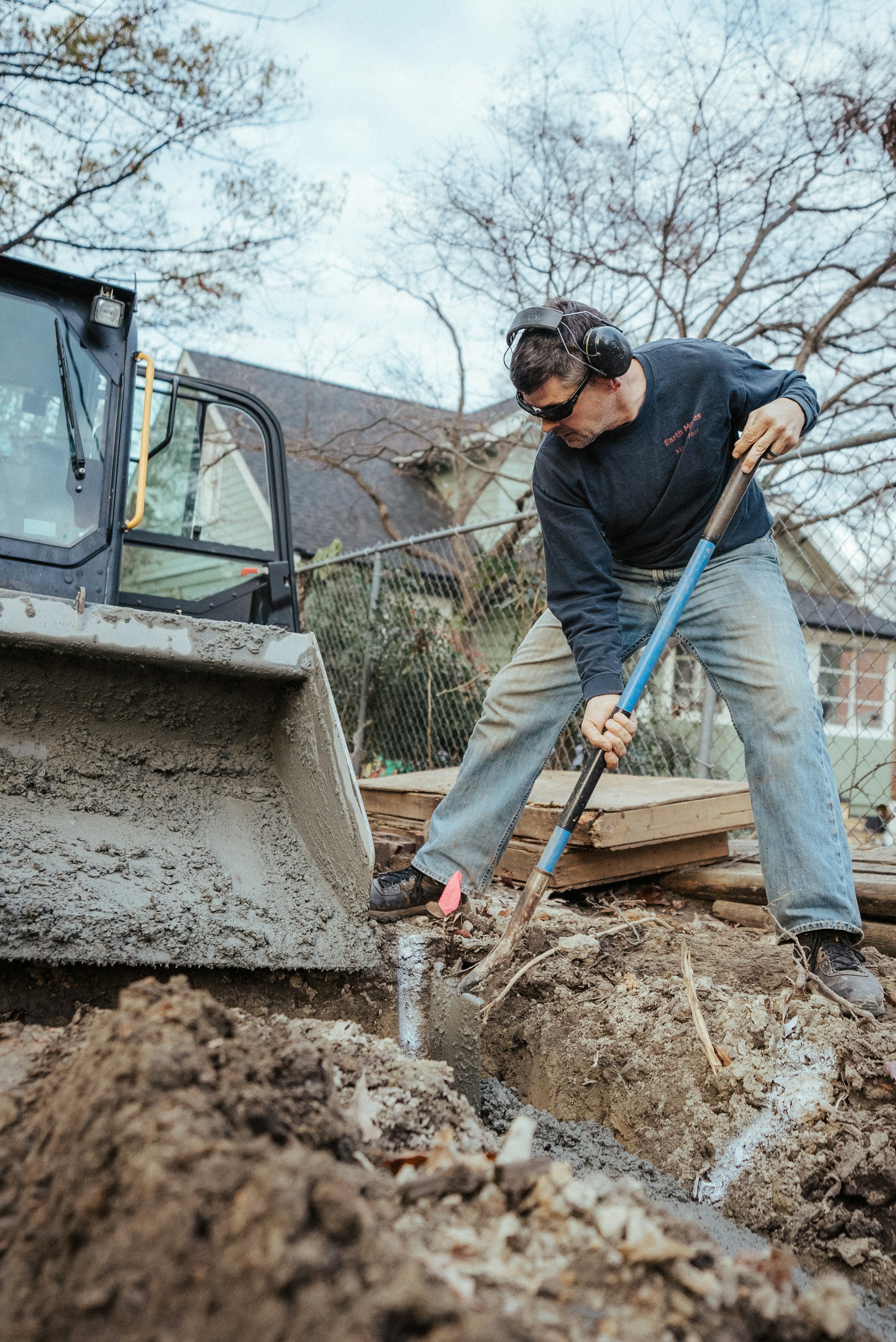 Ouvrier creusant une tranchée avec une pelle sur un chantier résidentiel.