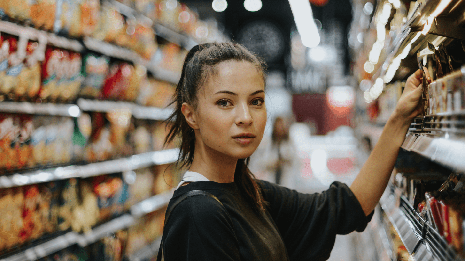 A woman selecting an item from a supermarket shelf
