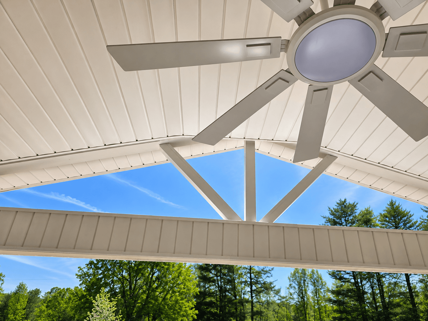 View from inside a covered front porch showing a vaulted ceiling, exposed beam, ceiling fan, and trees visible through the gable roof structure in Lewisville NC.