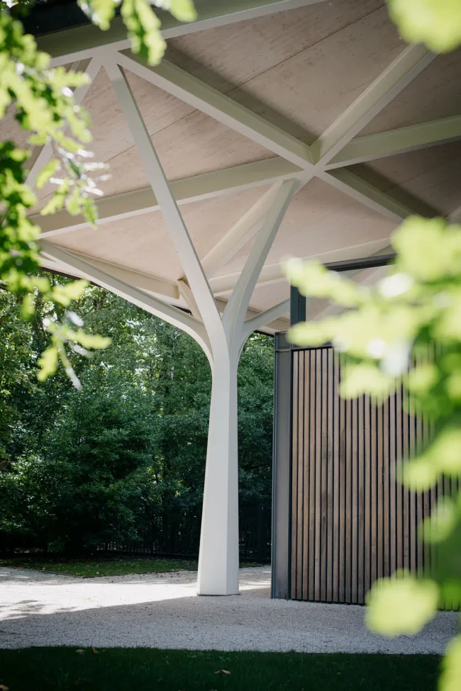 A modern structure with a large canopy supported by sleek pillars, surrounded by greenery.