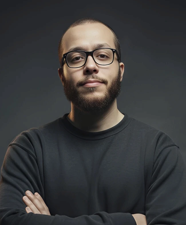Portrait of a young man with short hair, wearing a dark t-shirt, against a plain background.