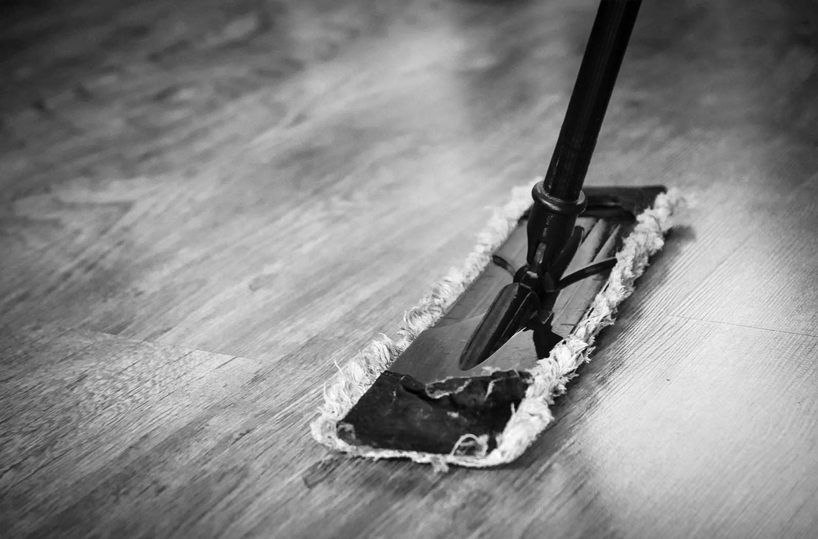 "A mop resting against a wooden floor, with the handle leaning slightly to the side. The scene suggests cleaning in progress or a recently cleaned area.