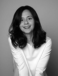 A black and white photo of a girl standing in front of a wall and smiling.