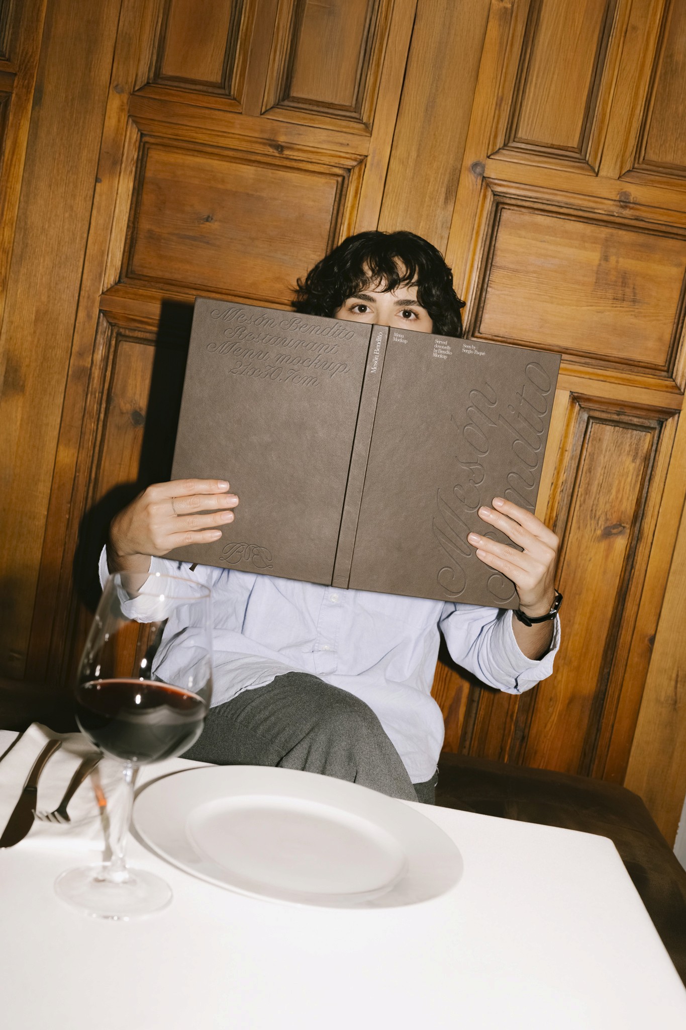 A restaurant diner hiding behind a large menu with a glass of red wine on the table