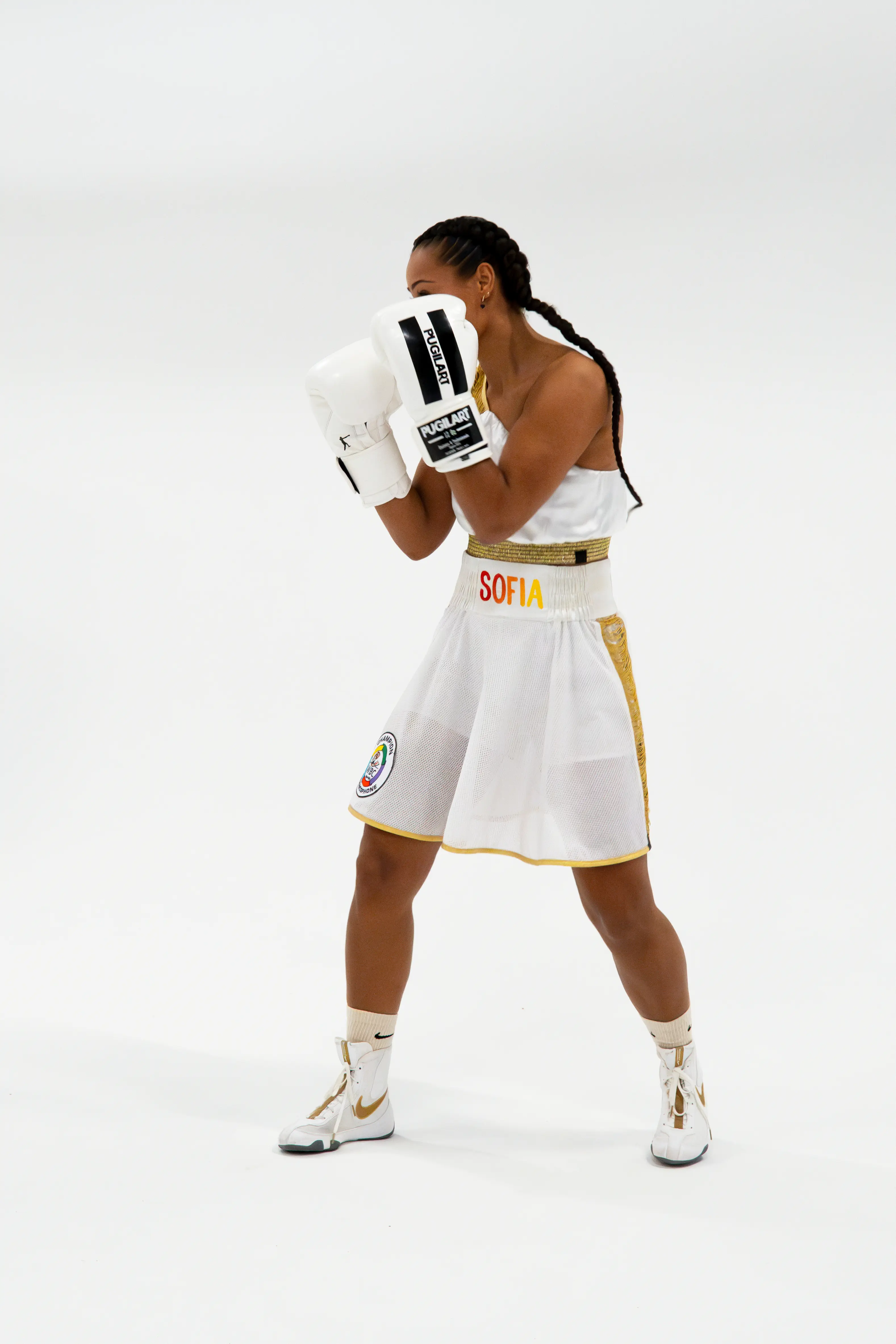 Female boxer Sofia Nabet supported by SNCF, wearing a white outfit and photographed in a fighting stance against a white studio background.