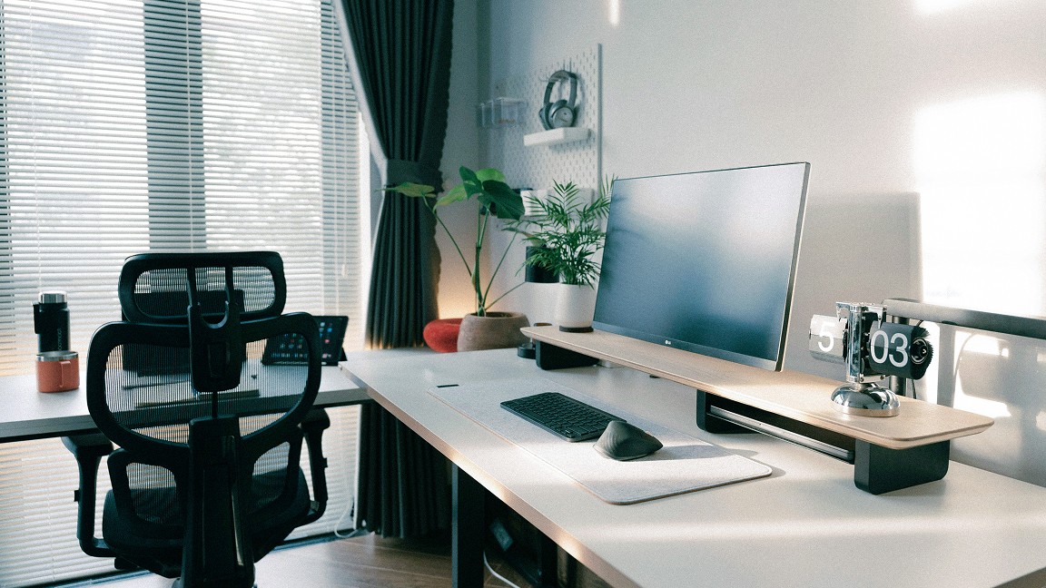 Großformatiges Foto eines minimalistischen Schreibtisch-Setups mit Monitor, Stuhl und Pflanzen am Fenster 