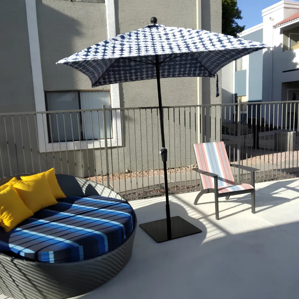 Modern patio furniture with blue striped daybed and patterned umbrella on a sunny deck.