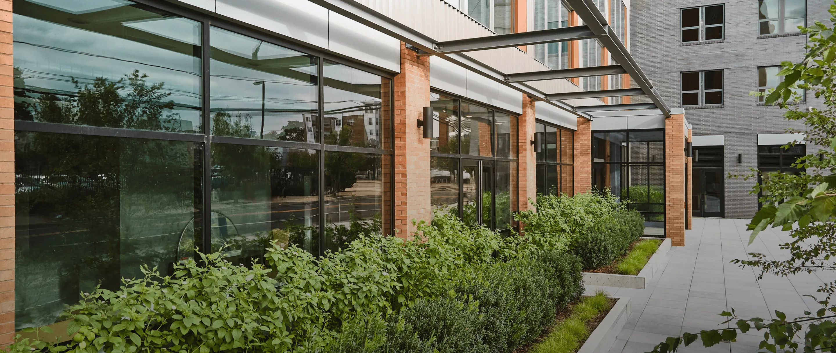 A modern building with glass walls, surrounded by greenery and a patio area. Natural light fills the space.