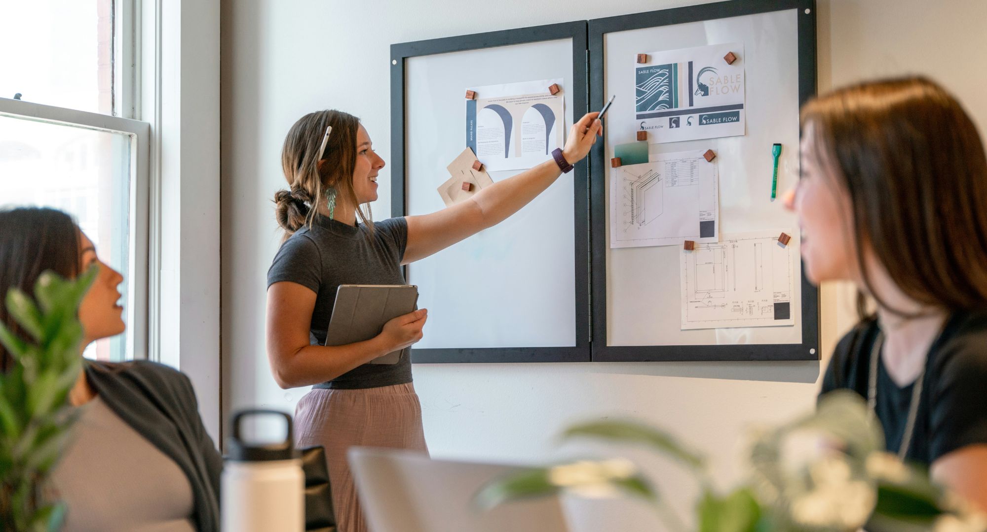 mulher empreendedora segurando notebook e apontando num quadro de anotações