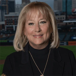 Denise Ilitch smiling in front of a Detroit ballpark backdrop