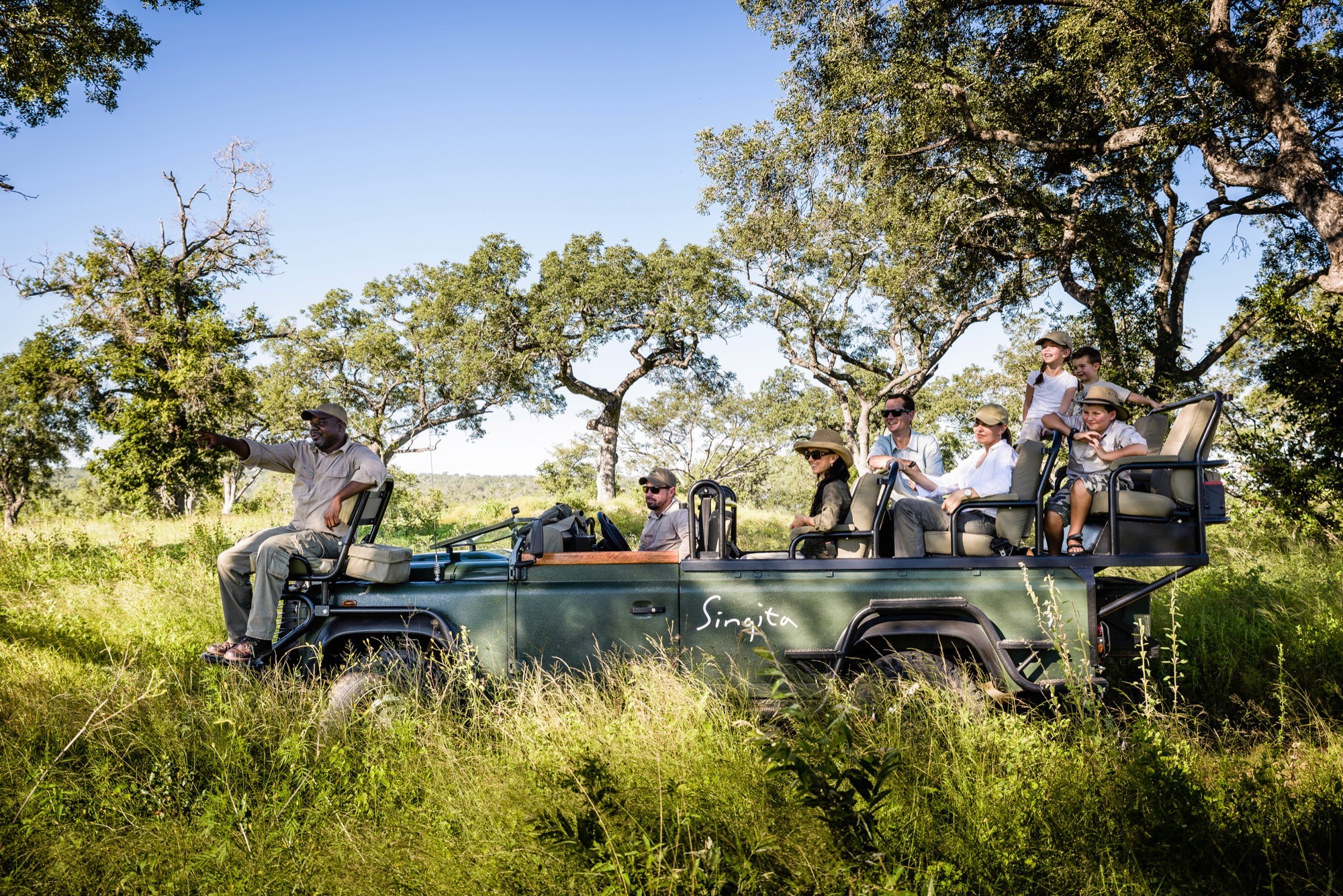 A guide pointing out game to a family aboard a Singita vehicle
