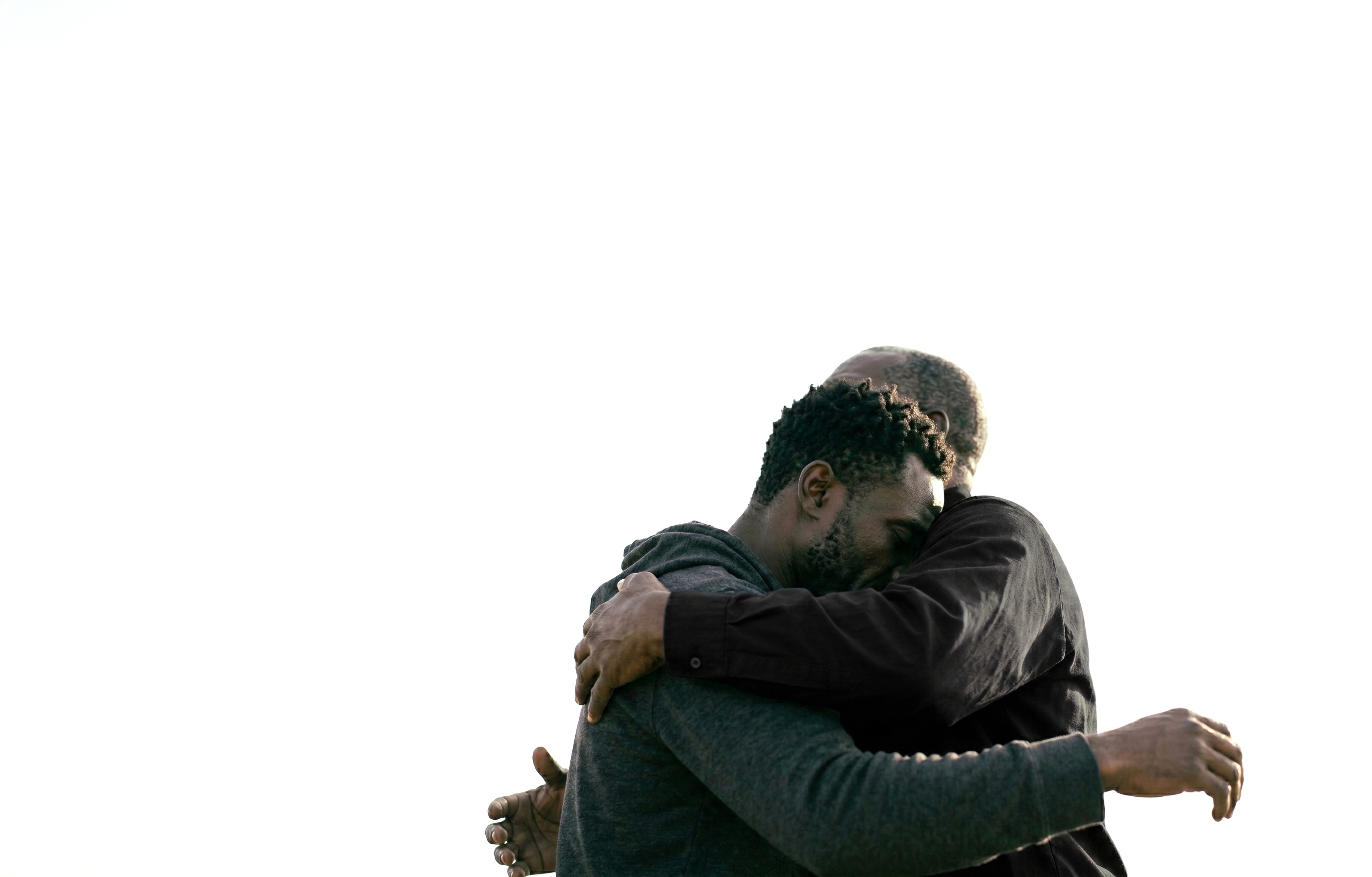 Two individuals share a heartfelt embrace against a plain white background, highlighting themes of connection, warmth, and emotional support.