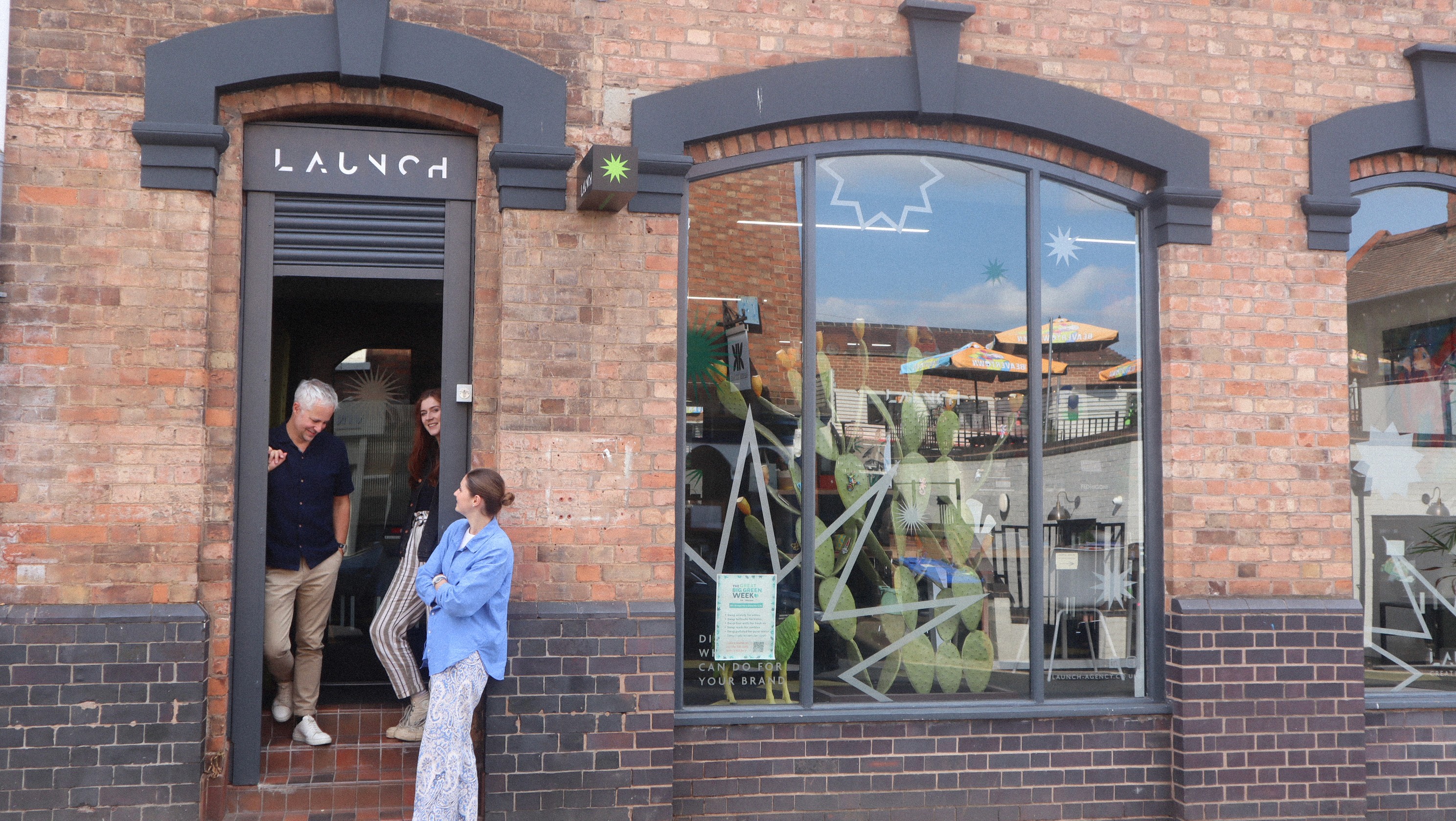 Launch agency employees smiling at a collaborative office table, seen through a window