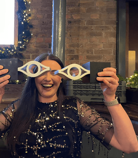 Team member smiling and holding up awards to look like novelty glasses shaped like eyes.