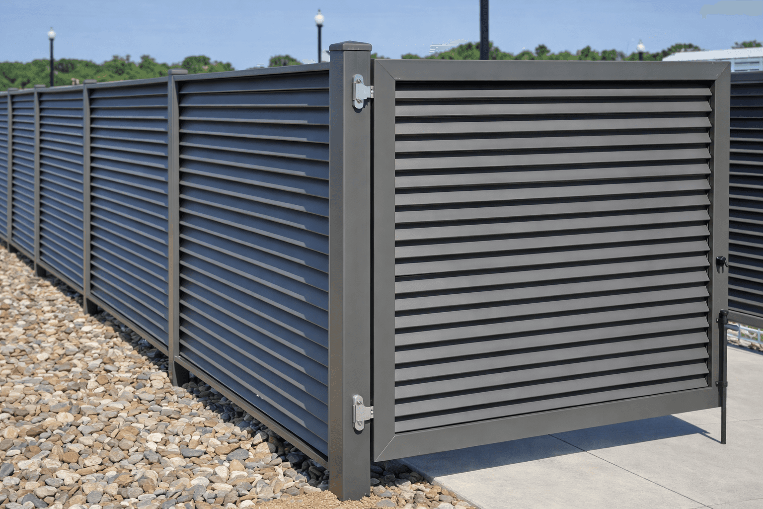 A close-up of a dark grey louvered aluminum privacy screen acting as a ground-level cover-up for outdoor commercial equipment.