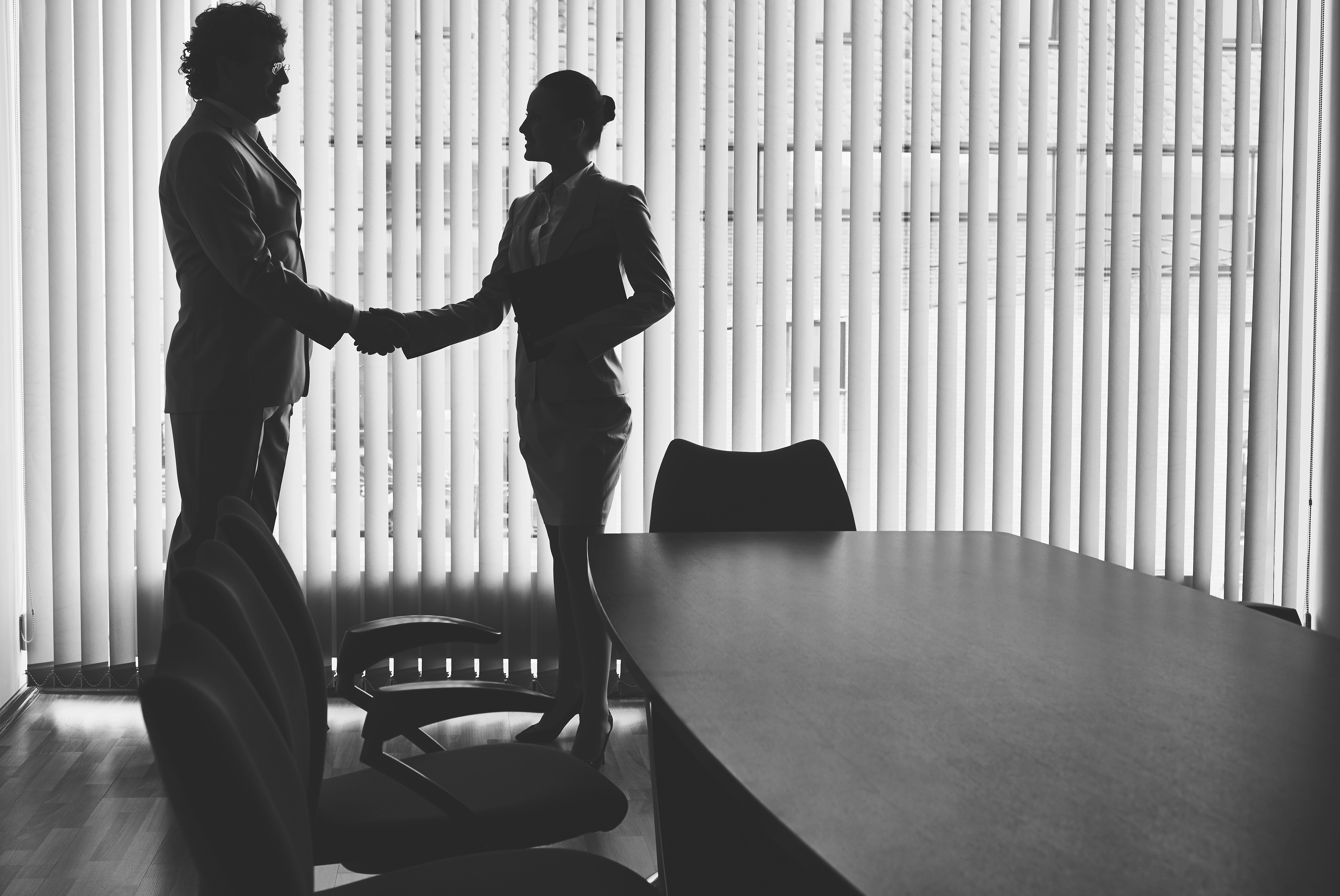 Two professionals shaking hands in a conference room, symbolizing business partnership.