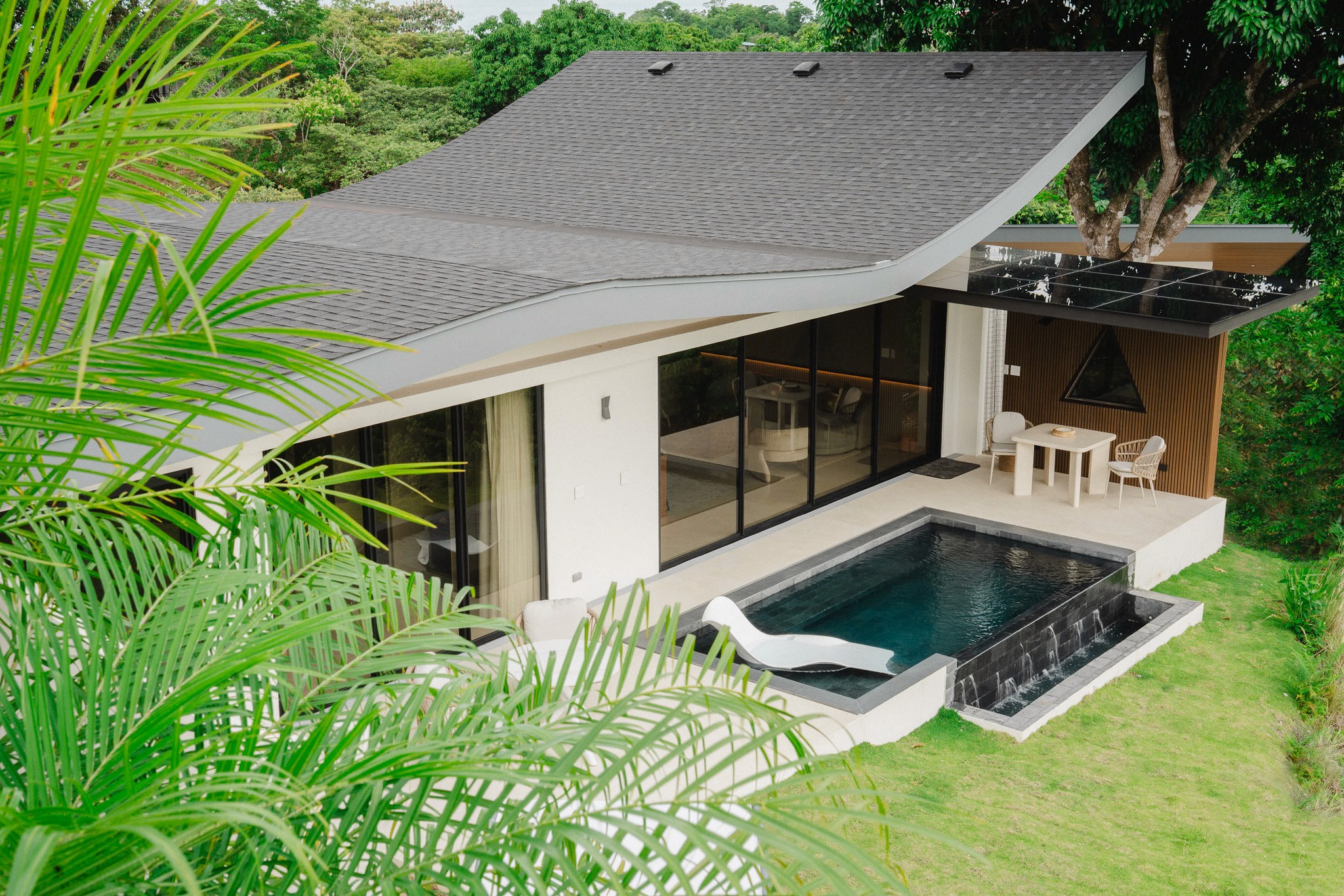 High-angle view of a Costa Rica vacation rental showing the cascading infinity pool, in-pool sun lounger, and lush surrounding rainforest.