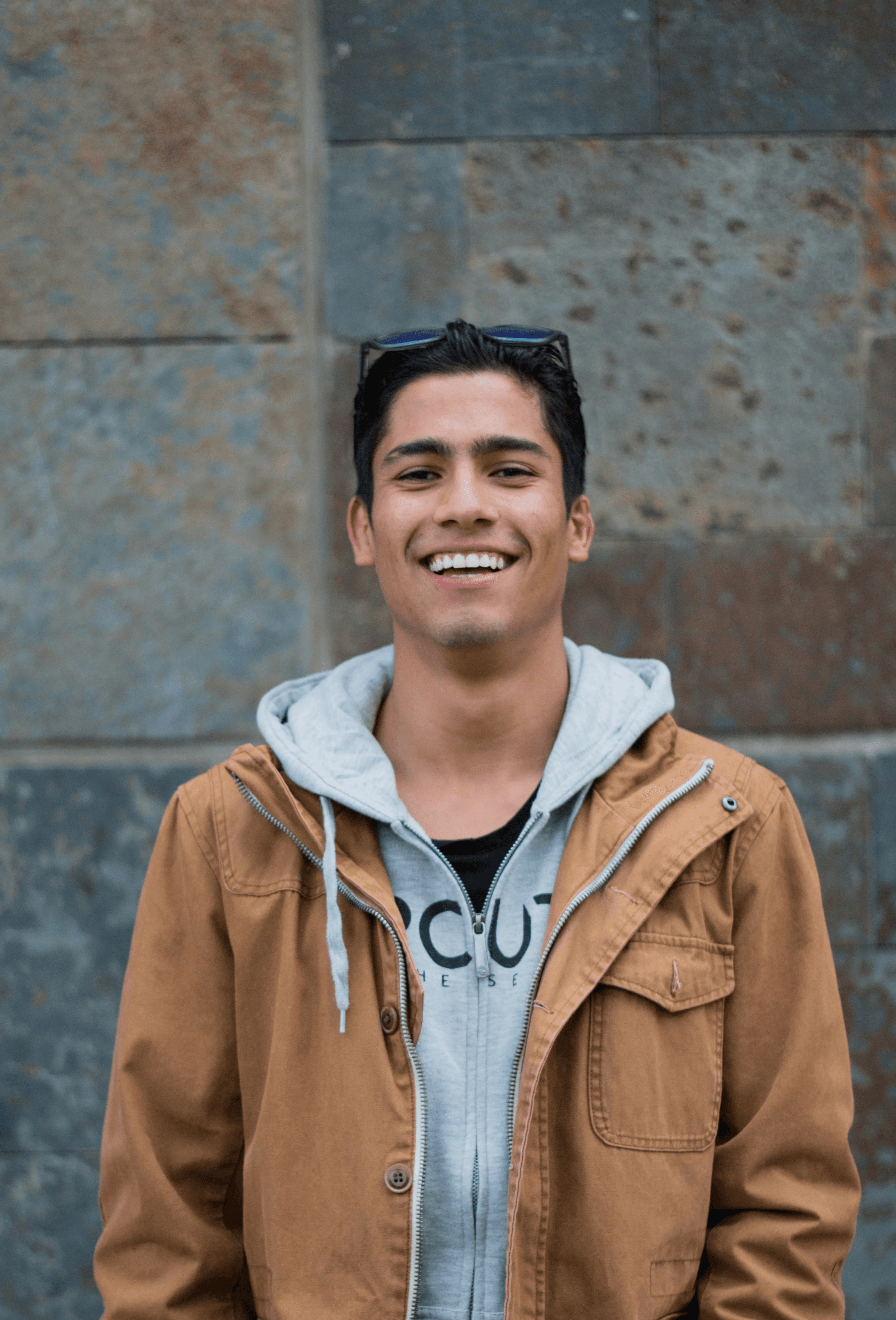 man in brown coat standing near concrete wall smiles
