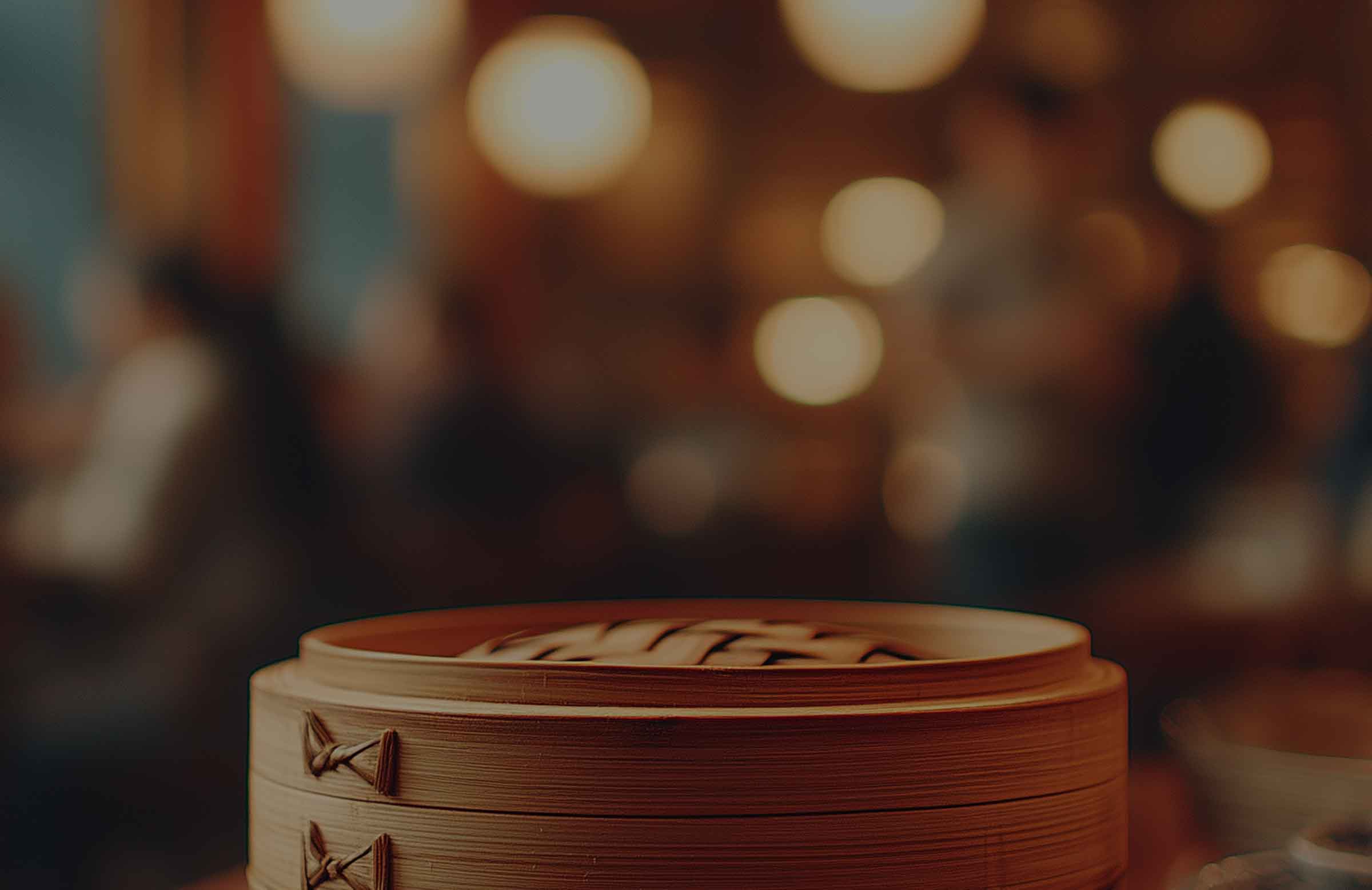 Stacked bamboo steamers on a table in a warmly lit restaurant with a blurred background of diners and ambient lighting.