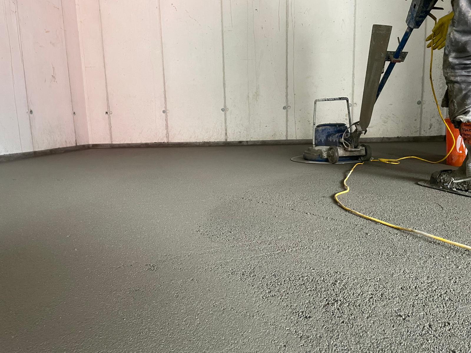 Ein Arbeiter glättet während einer Bauarbeiten mit einem Elektrowerkzeug einen Betonboden.
