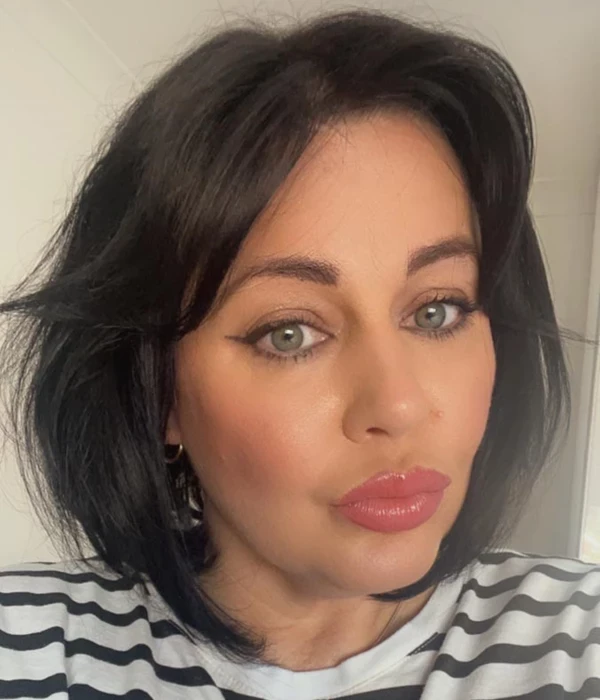 A person with shoulder‑length dark hair wears a black‑and‑white striped top indoors. The background is neutral and softly lit.