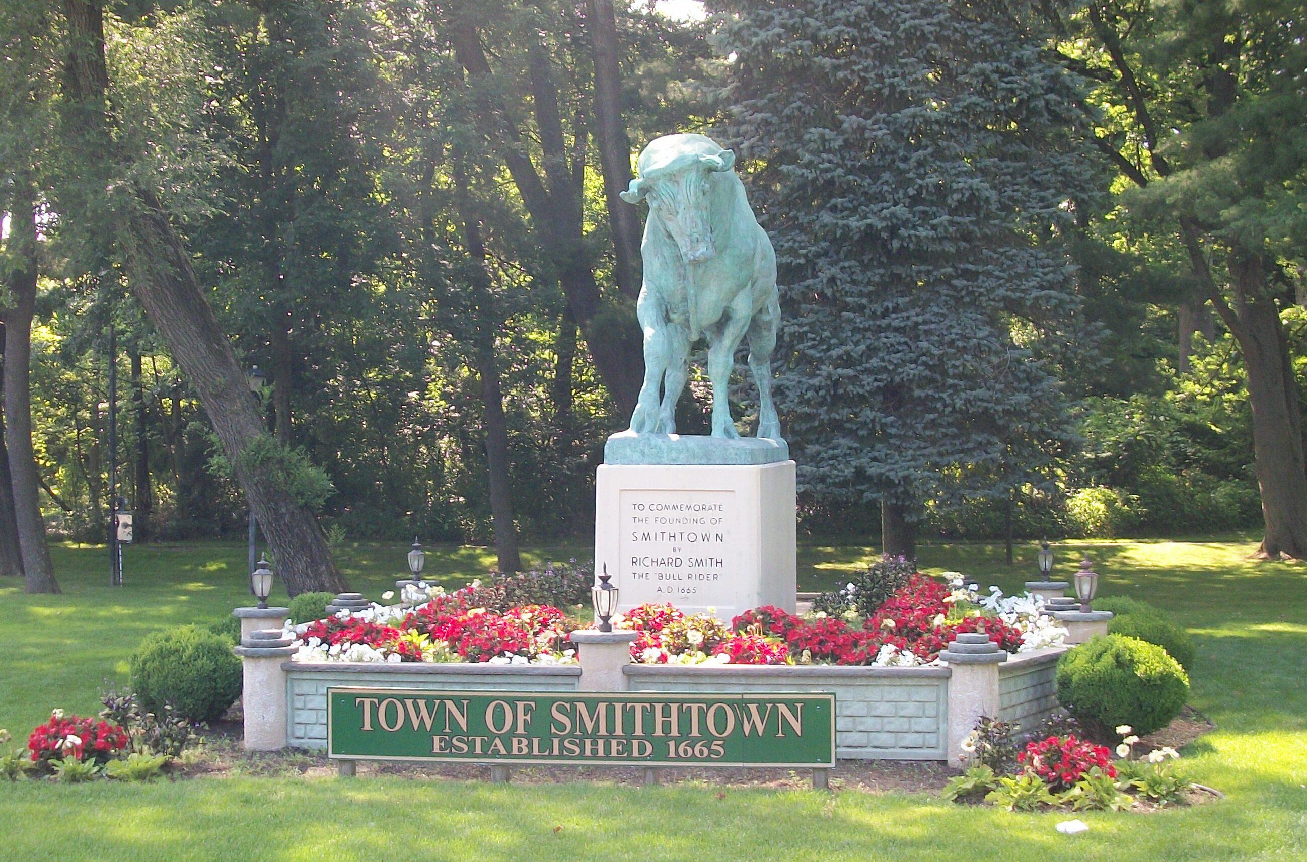 A bronze statue of a lion on a pedestal surrounded by colorful flowers in a green park setting.