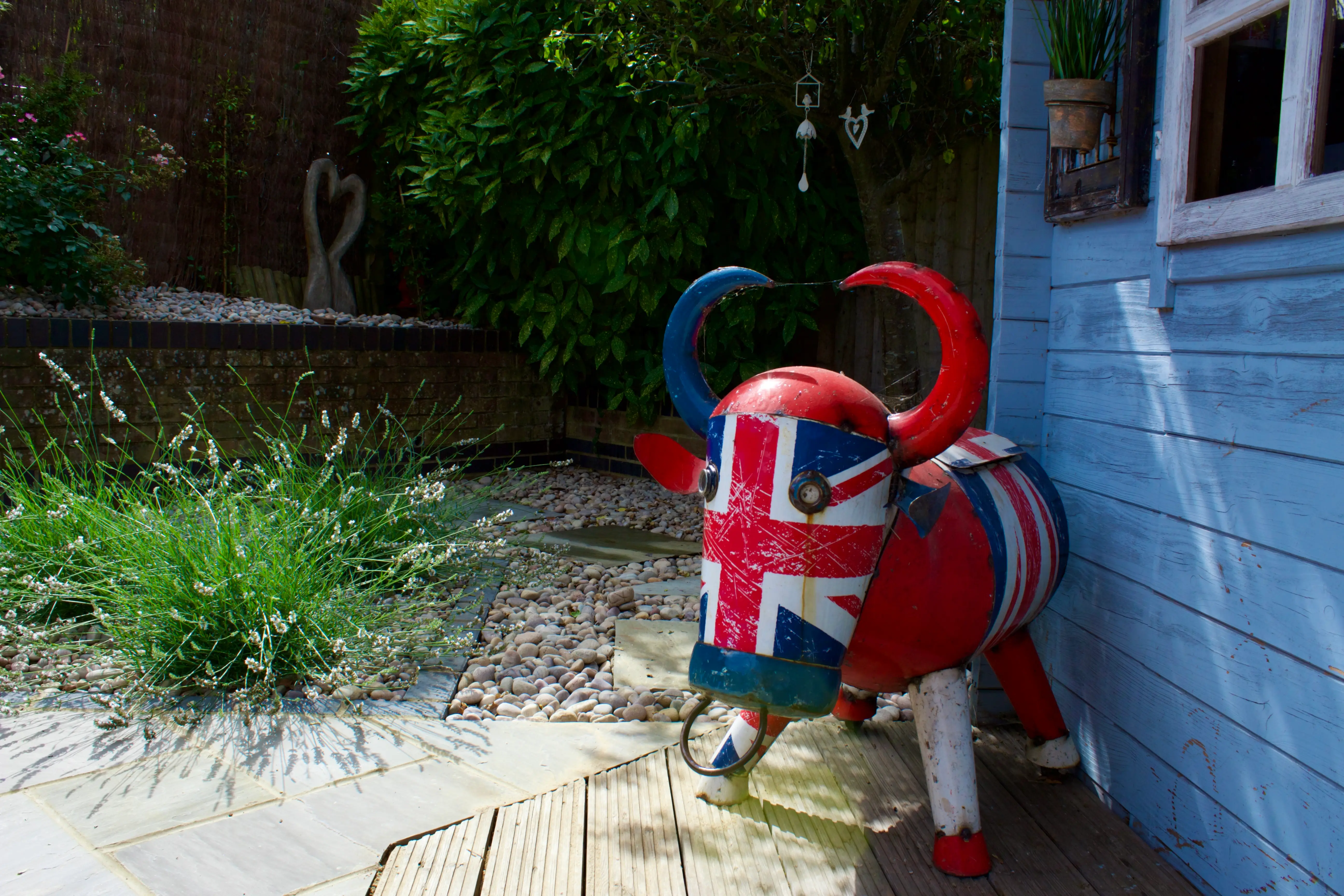 A colorful elephant sculpture painted with the Union Jack stands near a blue building amidst greenery.