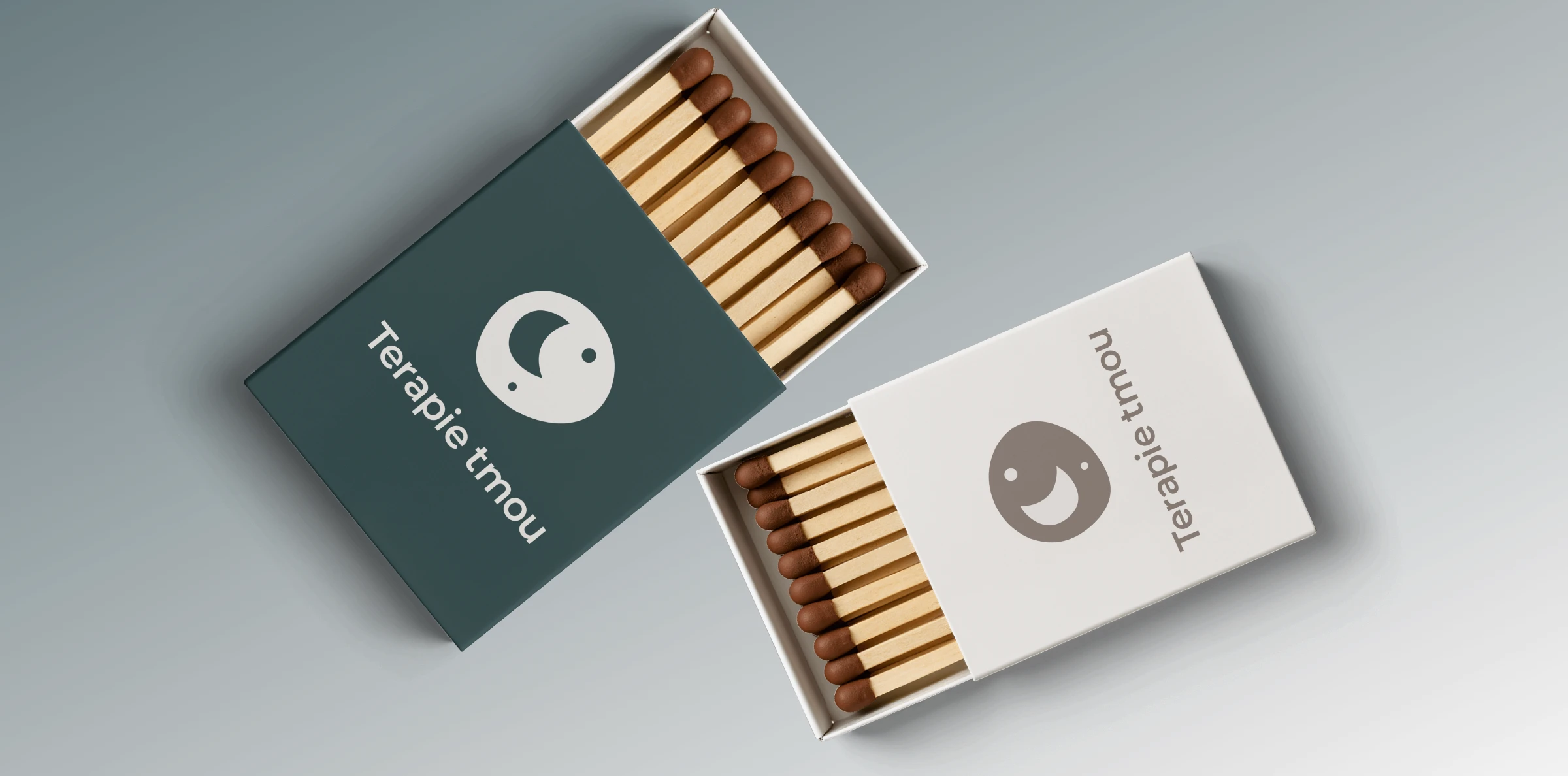 Návrh brandovaného merche 'Terapie tmou' – zápalky (krabičky) jako bonusový dárek pro klienty. Prezentace dvou barevných variant (tmavě tyrkysová a bílá) s minimalistickým logem v dark mode stylu