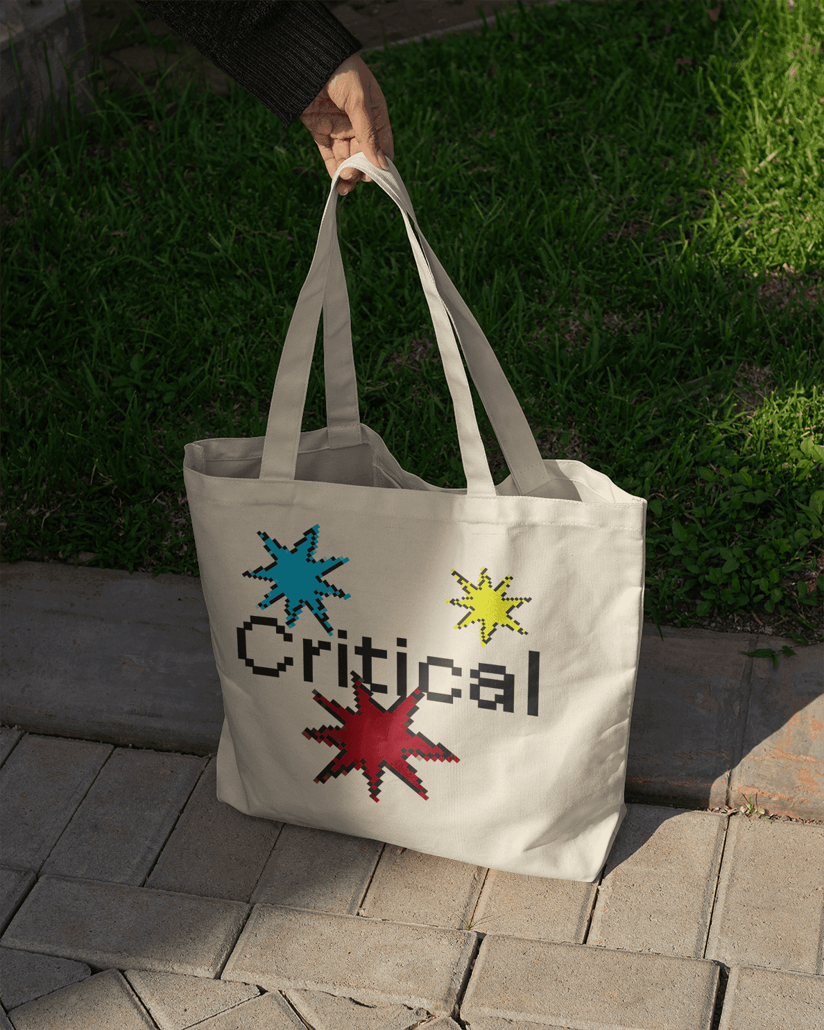 A tote bag with pixelated stars and texting saying "Critical" in the center