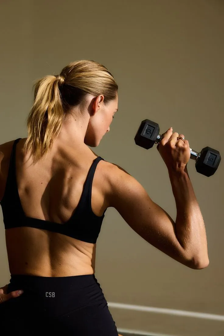 Woman lifting dumbbells during strength training workout, demonstrating  muscle engagement. Weeks 5-9 phase with intensity-focused exercises for  building tone and endurance.