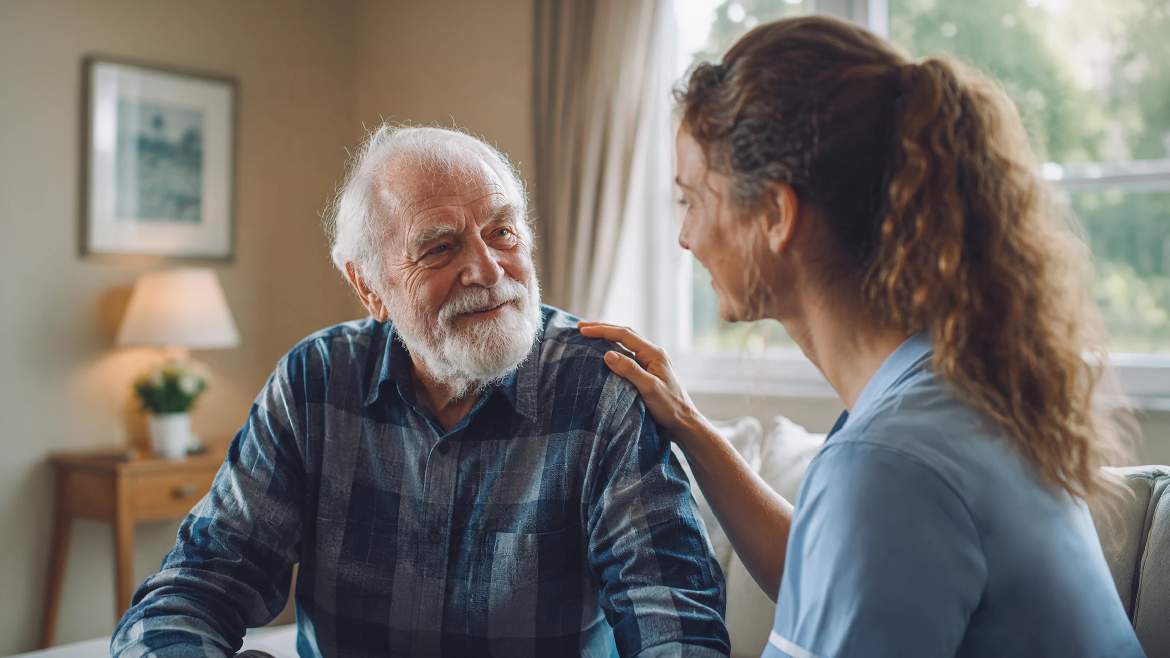 Support worker placing a reassuring hand on an older man's shoulder as they talk together in care home.