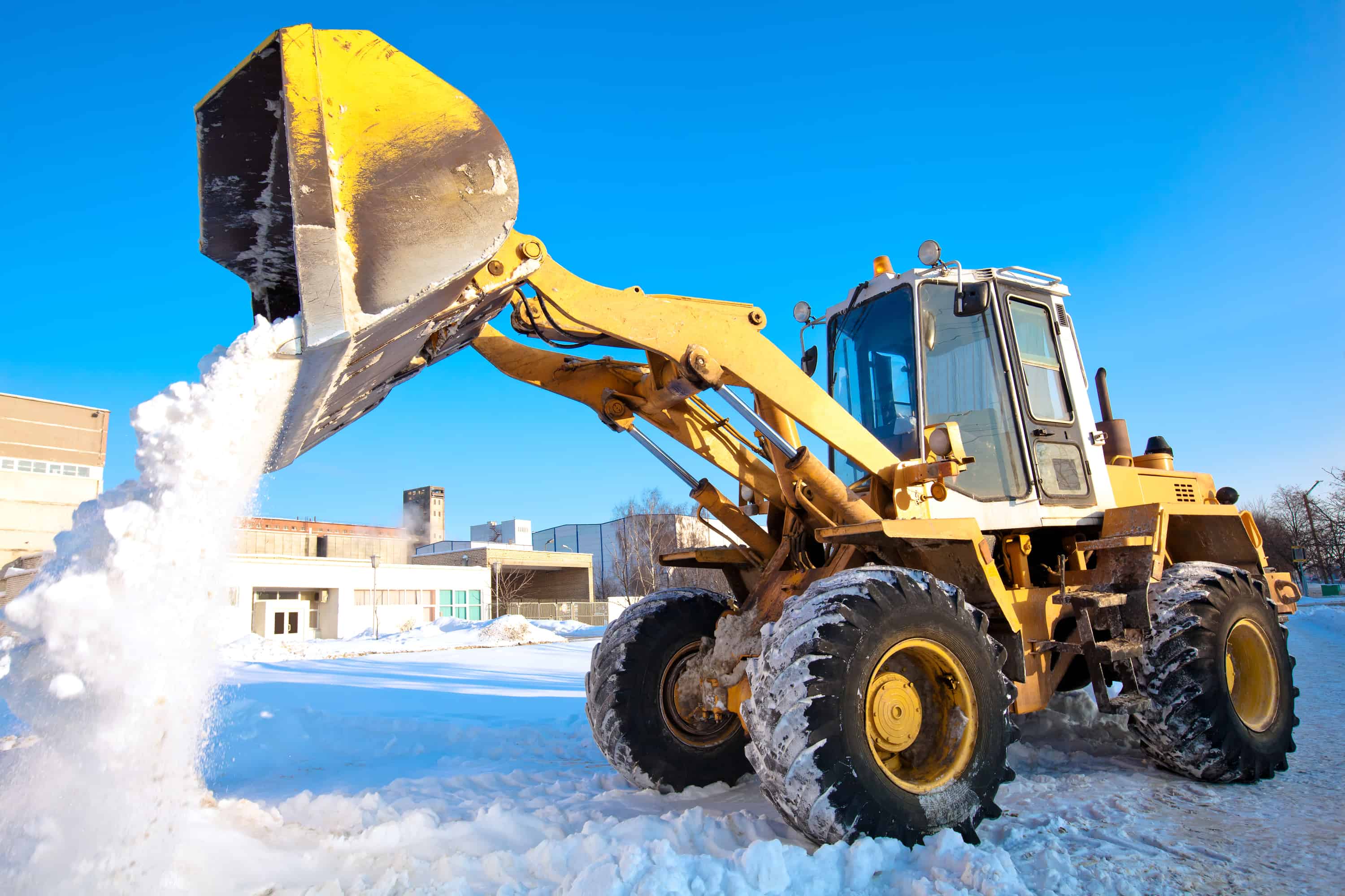 Wheel loader clearing snow from a frozen commercial site during winter
