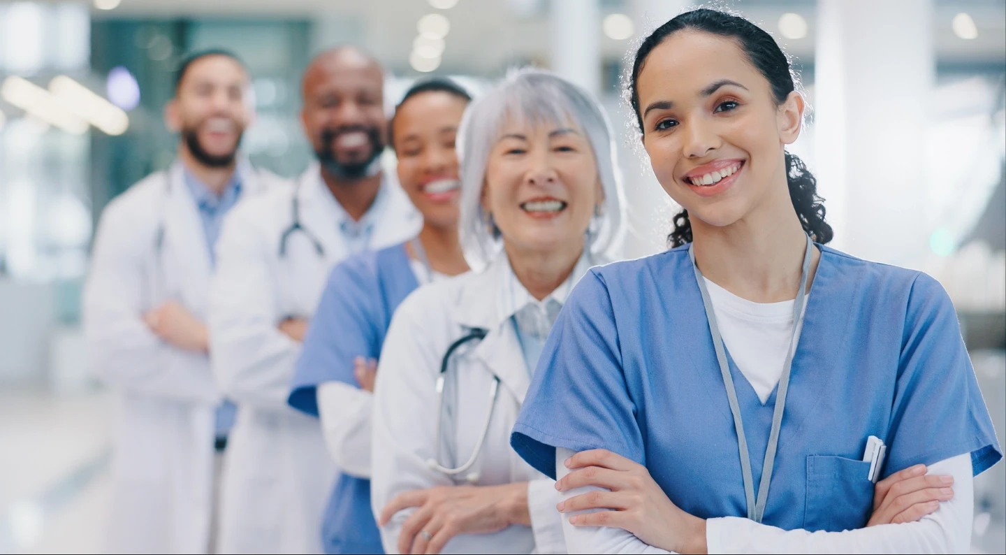 Diverse group of doctors standing in a line, with their arms folded, all smiling at the camera.