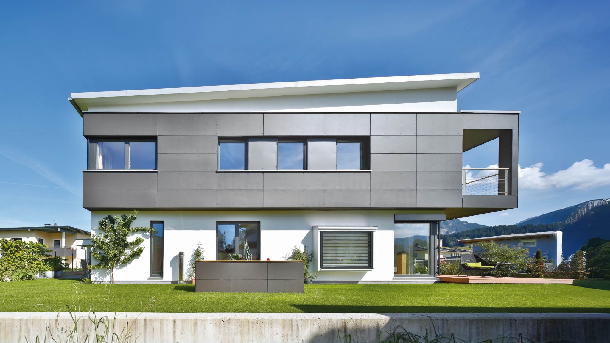 Modernes Einfamilienhaus mit geradliniger Architektur, großen Fenstern und einer grauen Verkleidung unter blauem Himmel.
