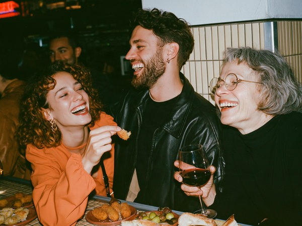 Three friends laughing together at a table with wine