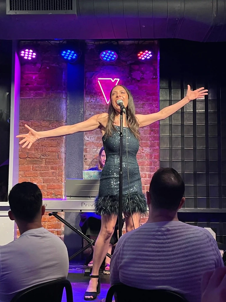 A performer sings with both arms flung wide during Little Miss Gorgeous