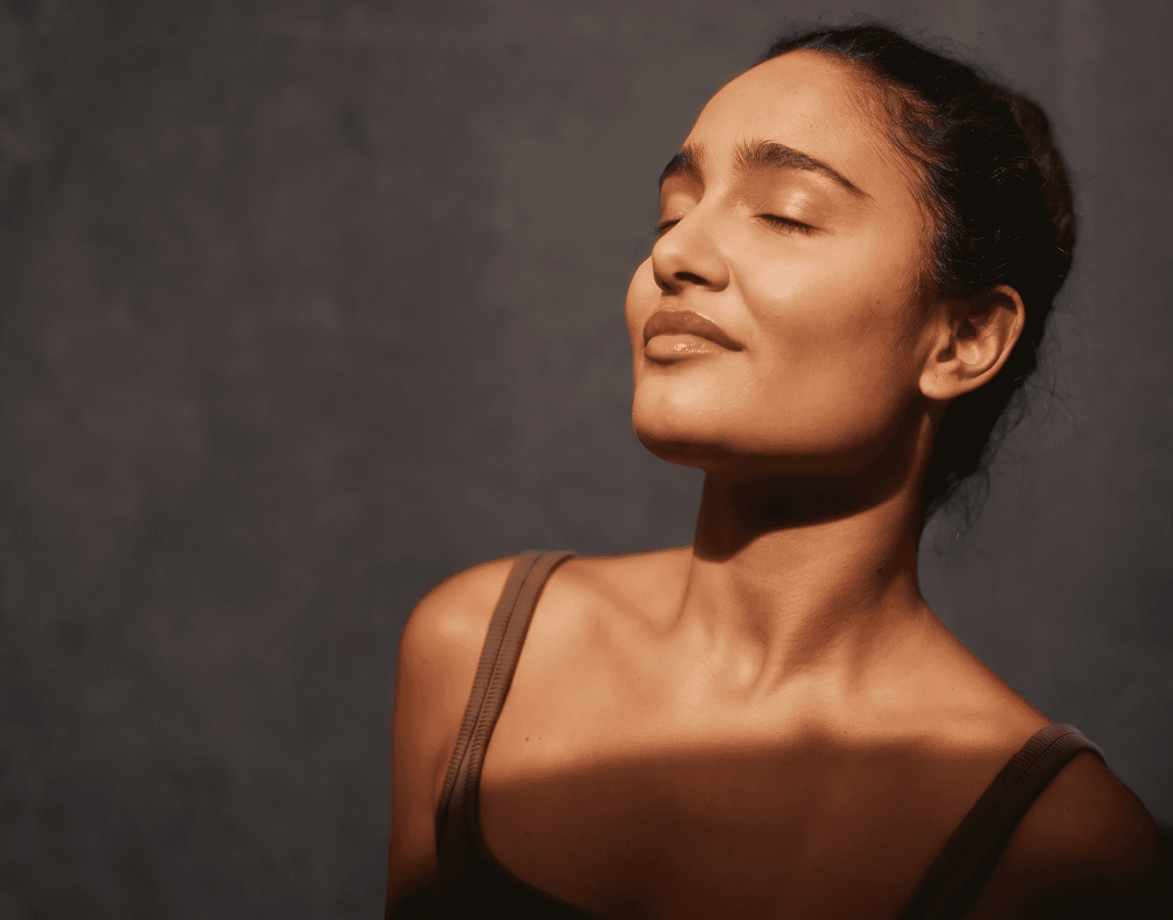 Close-up of a person’s neck and collarbone in warm sunlight, with soft window shadows creating a calm, intimate mood.