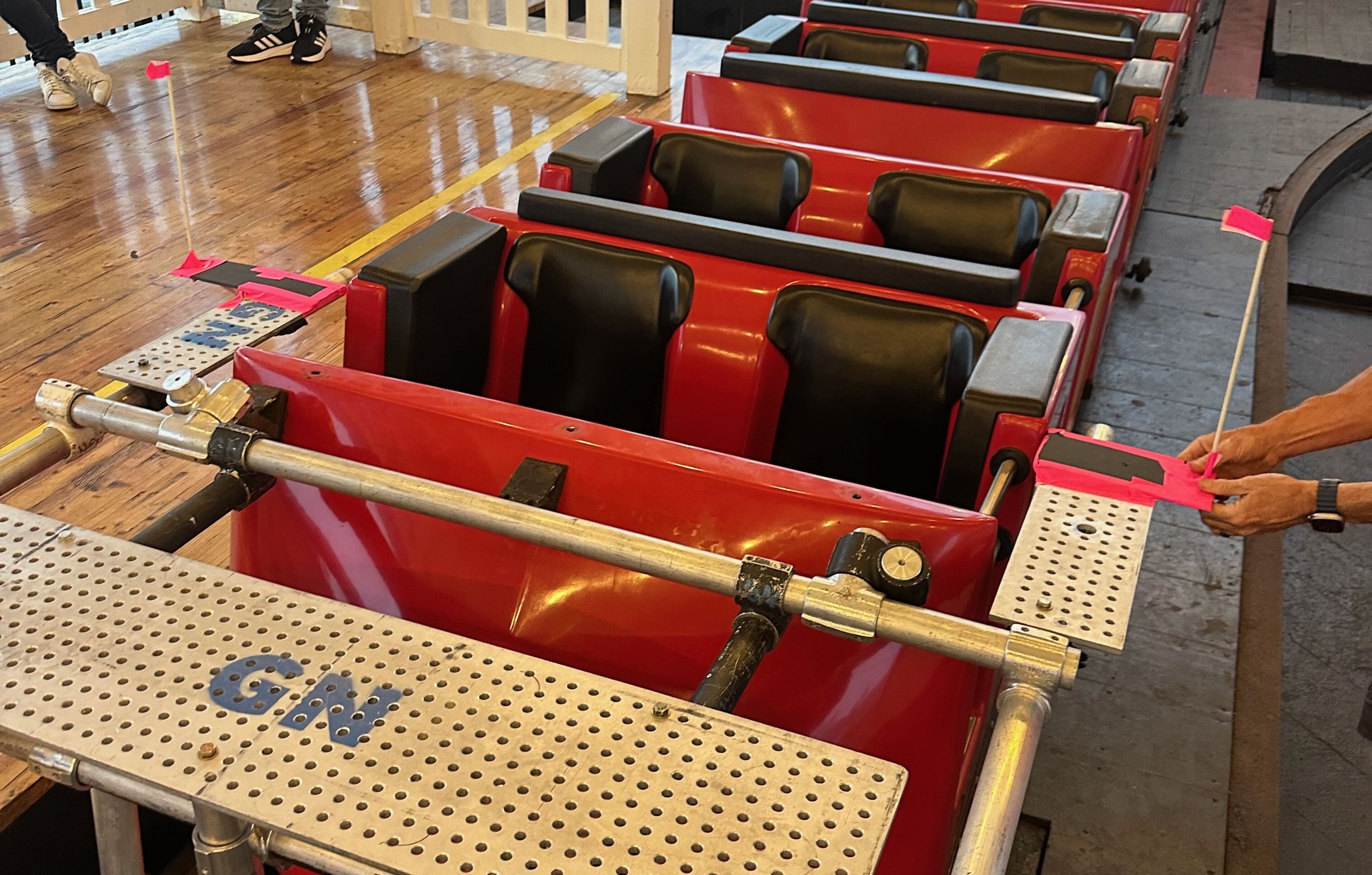 Grip crew building a speedrail cross-bracing camera rig on the front of a red wooden roller coaster car at Belmont Park in San Diego, with hardware and Hollaender fittings visible