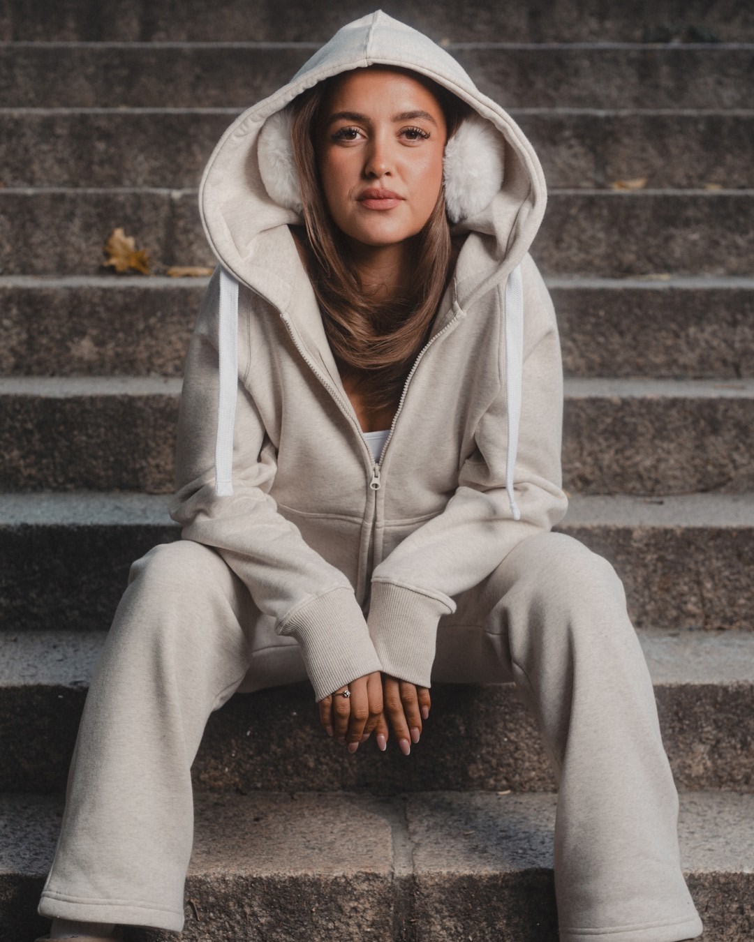 A model seated on stone steps wearing a full zip hoodie and sweatpants set, showcasing a complete loungewear look.